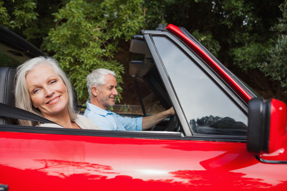 Side view of mature couple driving red convertible on bright day